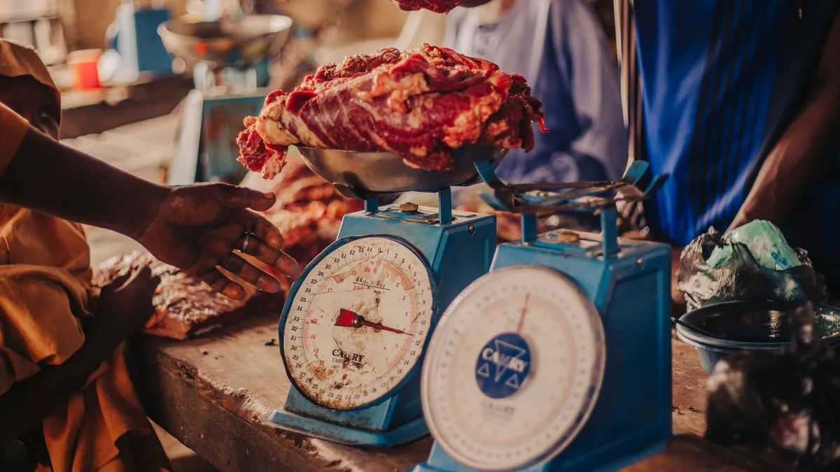 A person weighing a portion of food on a digital kitchen scale next to a plate of vegetables