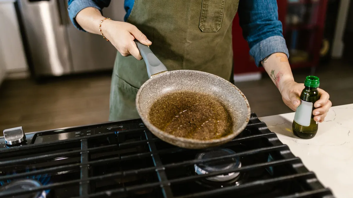 A person pouring olive oil into a frying pan while cooking at home
