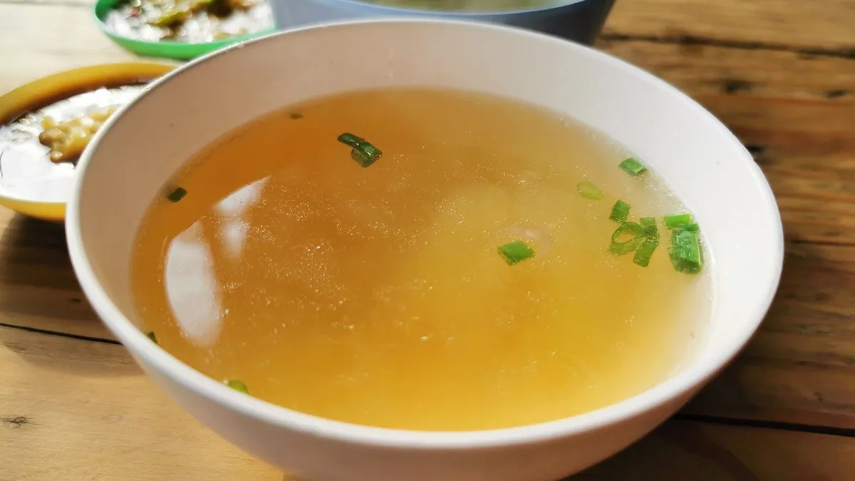 A steaming bowl of broth-based vegetable and lentil soup on a kitchen counter