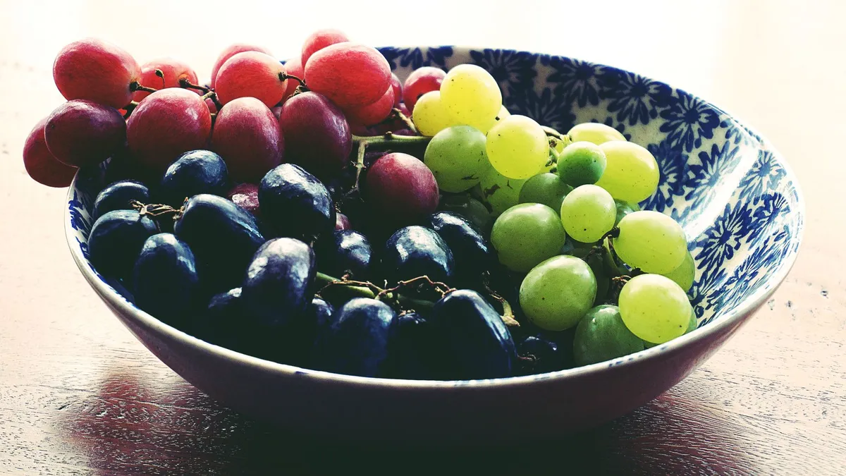 A bowl of fresh water-rich grapes next to a small handful of raisins