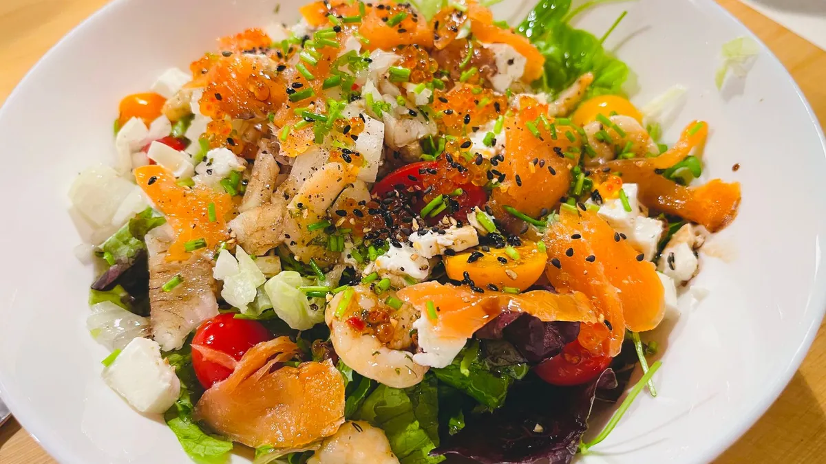 A large bowl of colourful mixed salad with vegetables and grilled chicken on a wooden table