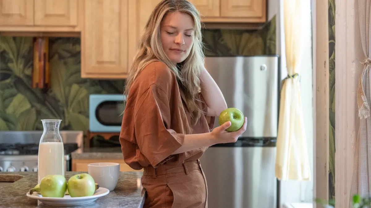 Une femme mordant dans une pomme entière avec la peau dans une cuisine lumineuse