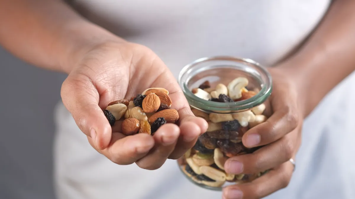A person taking a handful of mixed nuts from a jar while cooking