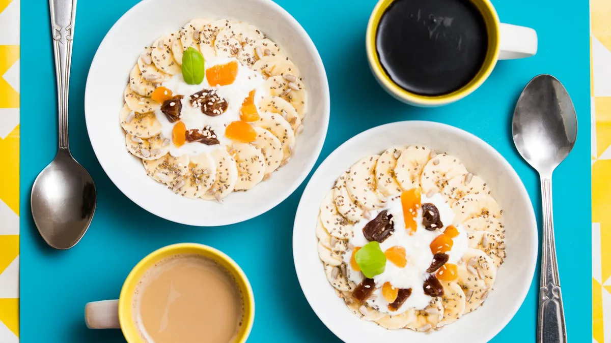A glass of kefir beside a breakfast bowl of yoghurt, berries and seeds