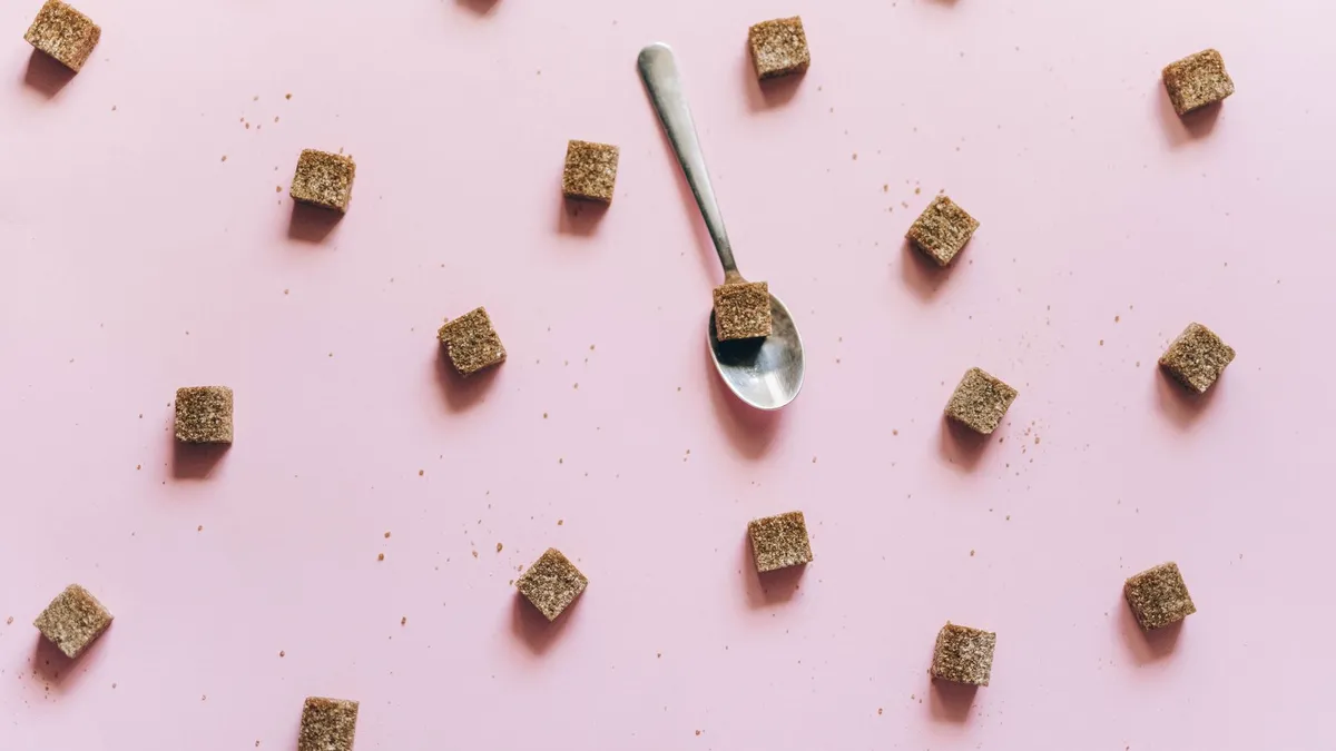 A wooden spoon holding white sugar next to scattered sugar cubes on a table