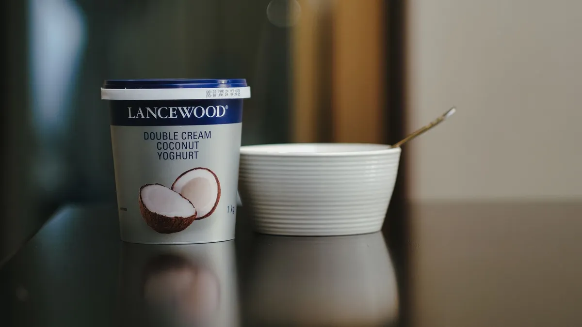Person checking the ingredients list on a yoghurt pot in a kitchen