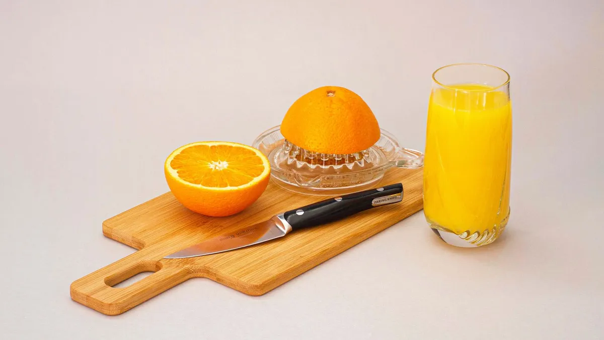 A glass of orange juice next to a breakfast plate on a wooden table