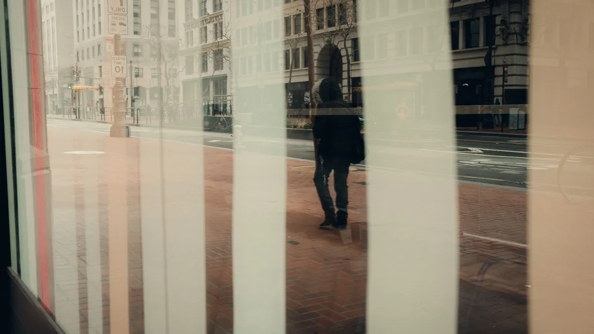 A person walking briskly along a city pavement carrying a bag, casual daytime movement