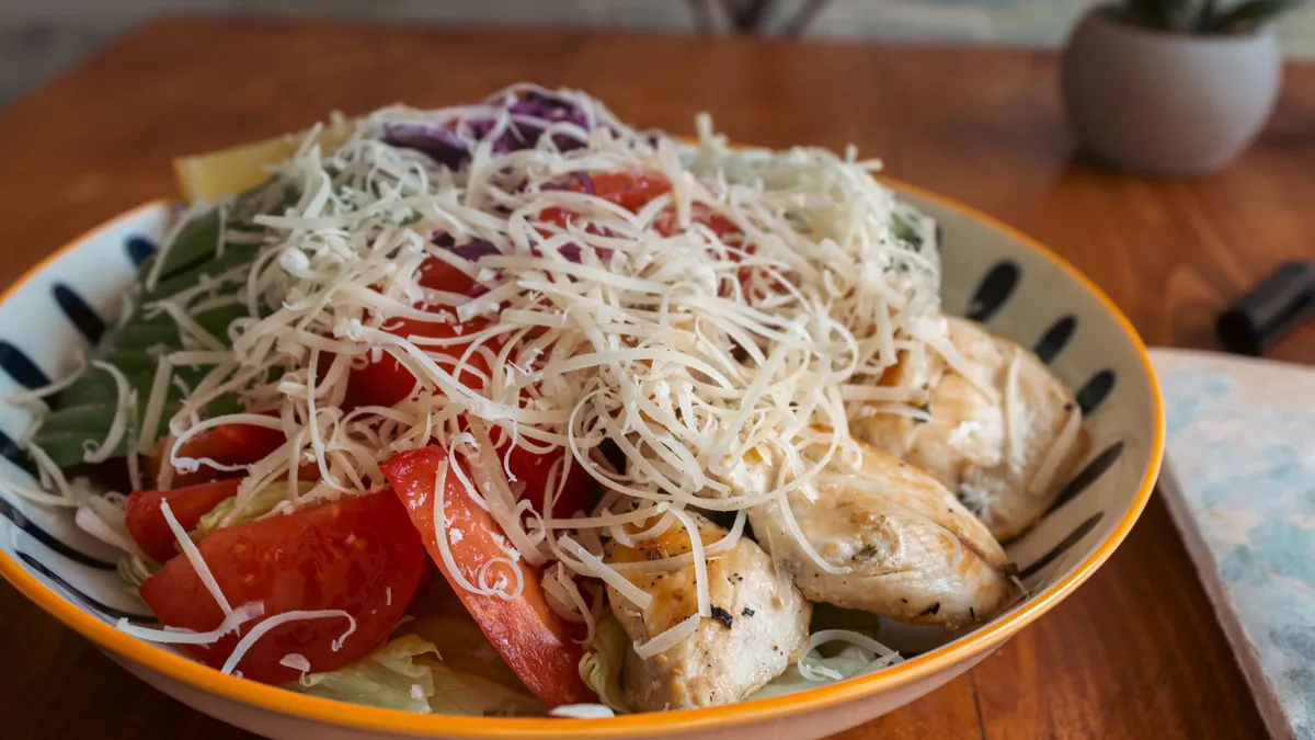 A plate of grilled chicken with mixed salad and vegetables on a wooden table