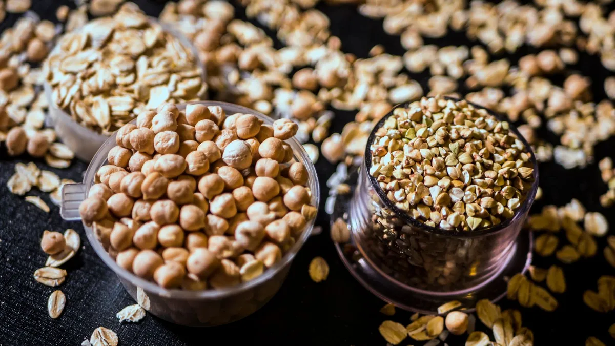 A wooden table with bowls of oats, lentils, chickpeas and fresh fruit