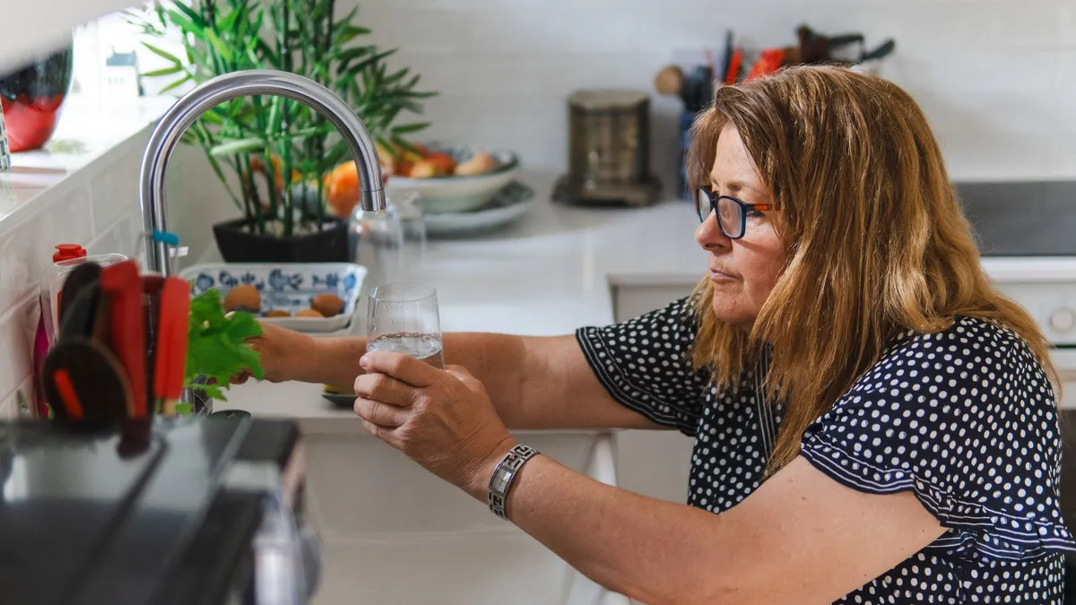 A person pouring a glass of water in a bright kitchen
