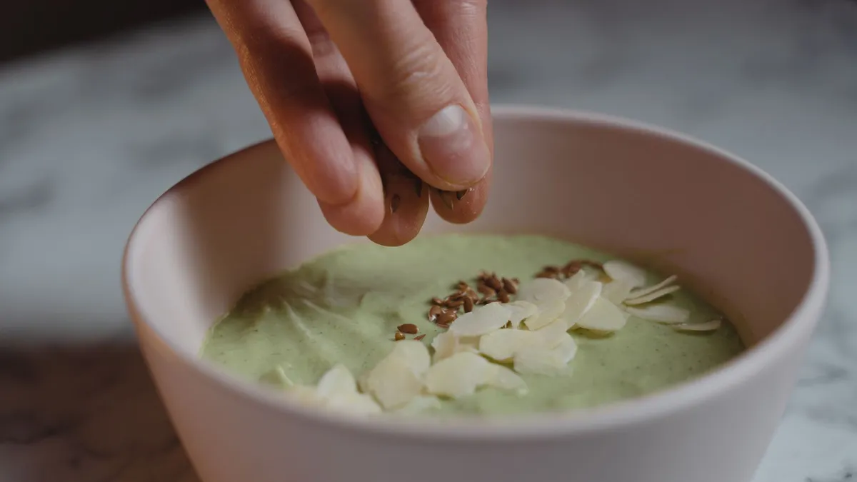 A person blending a protein smoothie with banana and milk in a bright kitchen